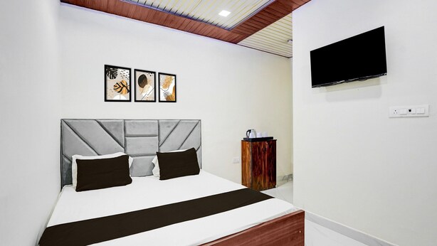A modern hotel room with a bed, a TV mounted on the wall, and artwork above the bed. - Deluxebhagwati Palace (Mathura)