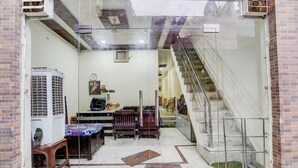 A room with a bed, a desk, a chair, a small table, a heater, a staircase, and a glass door. - Deluxebhagwati Palace (Mathura)