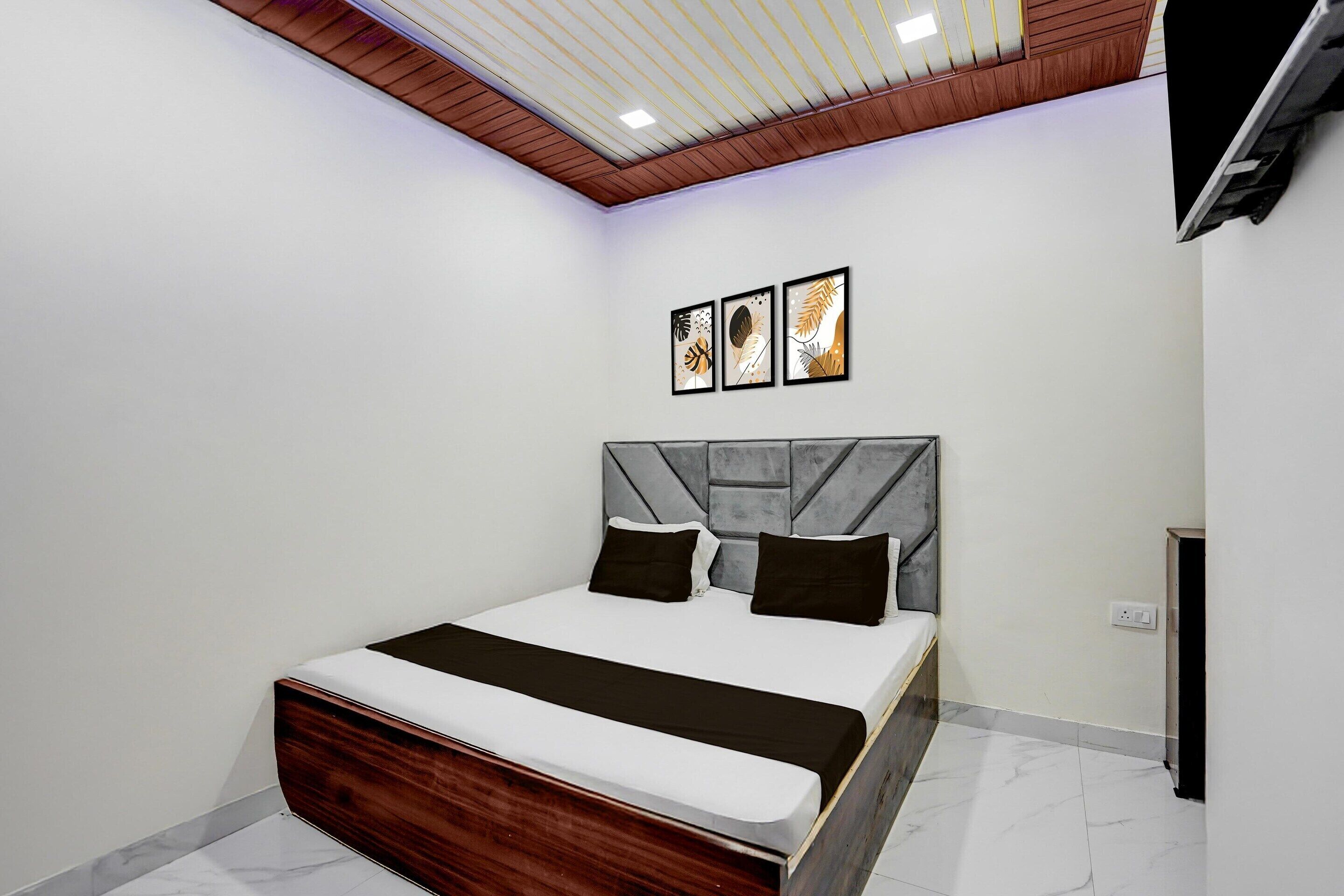 A bedroom with a bed, a headboard, a ceiling with wooden paneling, and three framed pictures on the wall.