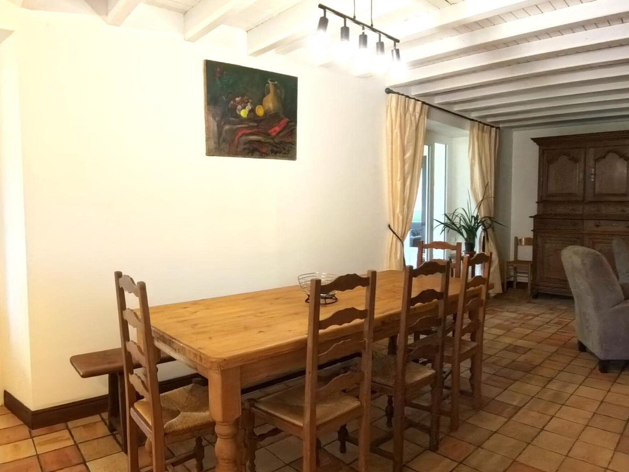 Un coin repas avec une table et des chaises en bois, un tableau accroché au mur et un grand meuble.