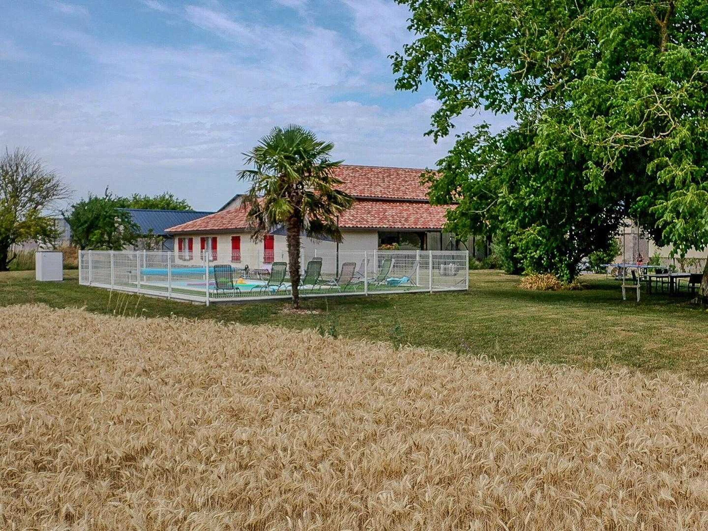 A house with a swimming pool, a fenced patio area, and a field in the foreground.