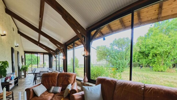 A spacious room with a high ceiling, large windows, a brown leather sofa, and a dining area. - Cottage with private pool - 4 guests (Vanxains)