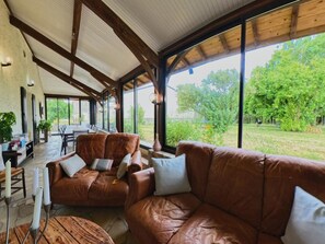 A spacious room with a high ceiling, large windows, a brown leather sofa, and a dining area. - Cottage with private pool - 4 guests (Vanxains)