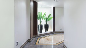 Un couloir doté d’un sol en marbre, d’une plante en pot et d’une fenêtre avec des stores.