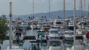 Een jachthaven met diverse boten afgemeerd, een heldere lucht en een bergketen in de verte.