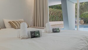 Hotelkamer met een groot bed, twee kussens, twee opgerolde handdoeken en twee welkomstkaartjes op het bed.