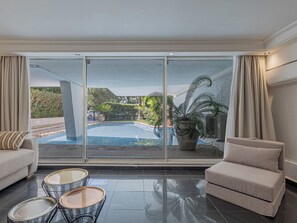 Ein modernes Wohnzimmer mit einem großen Schiebeglasfenster zum Poolbereich, einem Sofa, einem Couchtisch und einer Topfpflanze.