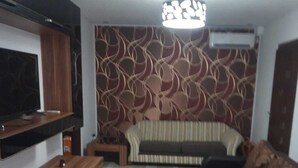 A modern living room with a flat-screen TV, a sofa, a patterned wall, and a ceiling light fixture.