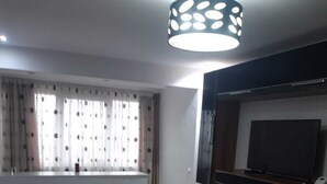 A living room with a sofa, a TV mounted on the wall, a wooden cabinet, and a patterned curtain.