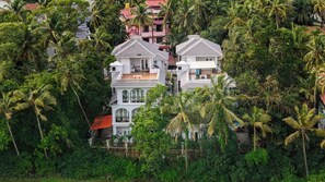 A multi-story building with a tiled roof, surrounded by dense greenery and palm trees. - ELIVAAS Casa Ritzy 5 BHK Villa & Pool  (Calangute)