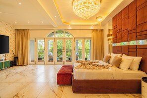 A spacious bedroom with a large bed, a television, and a view of greenery through the glass doors. - ELIVAAS Casa Ritzy 5 BHK Villa & Pool  (Calangute)