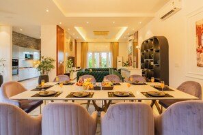 A dining area with a table set for four, a green sofa, and a kitchen in the background. - ELIVAAS Casa Ritzy 5 BHK Villa & Pool  (Calangute)
