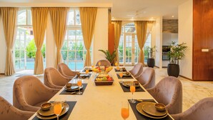 Comedor con una larga mesa dispuesta para una comida, rodeada de sillas y vista a zonas verdes.