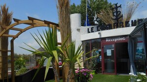 A reception area with a wooden archway, potted plants, and a sign reading 'LE COCORRE'. - Accessible mobile home, terrace - 6 guests (Lattes)