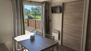 A room with a wooden table and chairs, a TV mounted on the wall, a sliding door, and a view of a balcony with a wooden railing. - Accessible mobile home, terrace - 6 guests (Lattes)