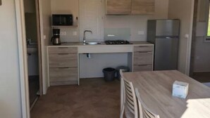 A compact kitchen with a sink, stove, and refrigerator, a small dining table with chairs, and a trash bin. - Accessible mobile home, terrace - 6 guests (Lattes)