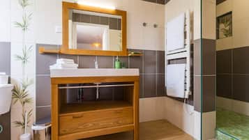 Un baño con tocador de madera, espejo, toallero y zona de ducha.