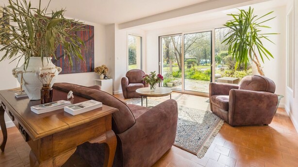 A modern living room with a wooden coffee table, two brown armchairs, a large vase with dried flowers, and a view of a garden through large sliding glass doors. - Room with private terrace (Guérande)