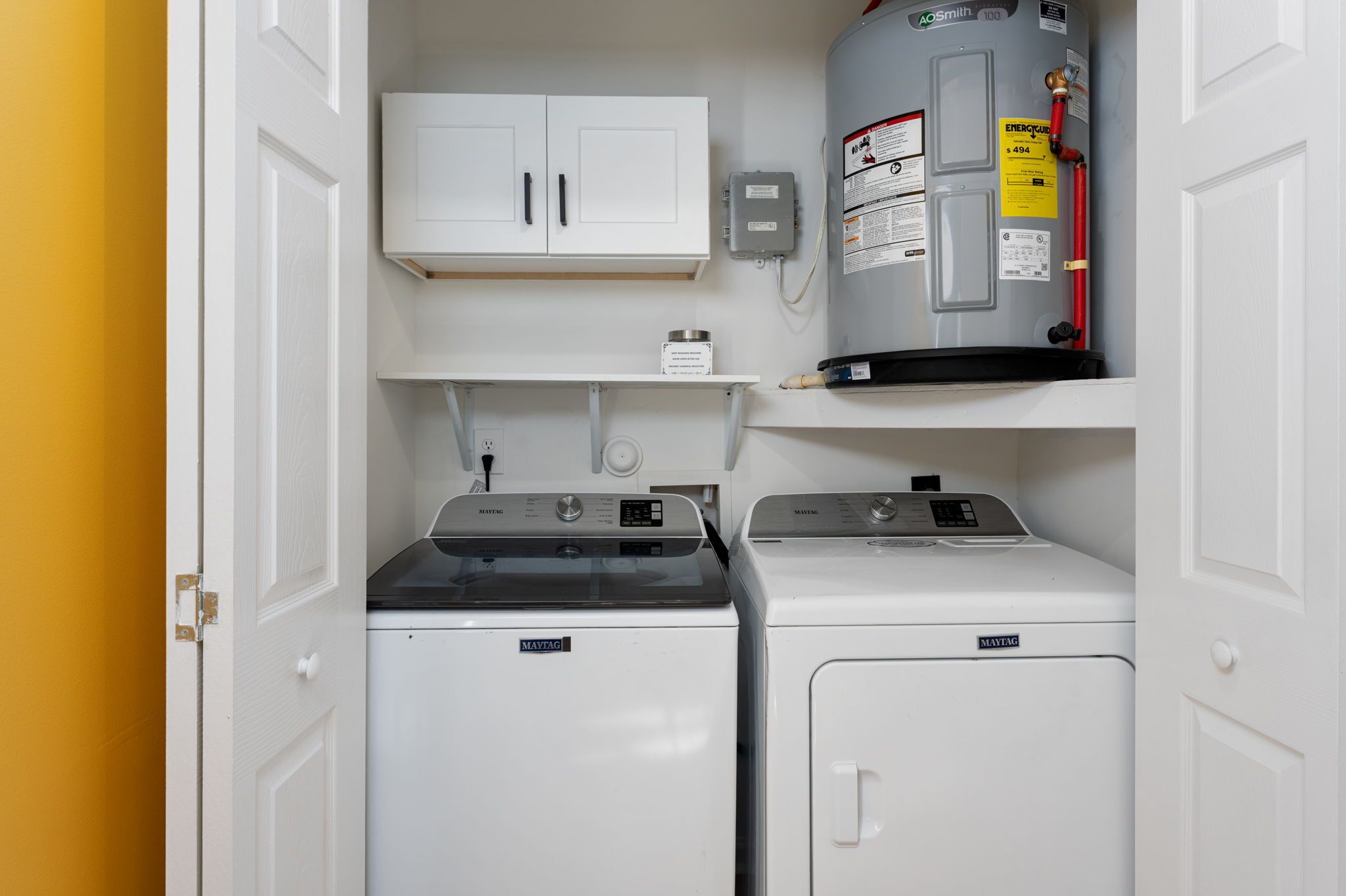 Une buanderie équipée de deux lave-linge Maytag, d’un chauffe-eau et d’un meuble de rangement au-dessus des sèche-linge.