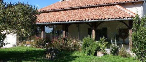 A house with a tiled roof, a covered porch, and a garden with various plants.