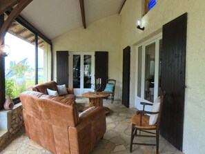A covered patio area with a leather sofa, a wooden chair, and a small table with candles.