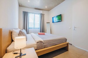 Un dormitorio moderno con cama, lámpara de noche y televisión montada en la pared.