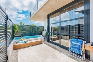 Un área de piscina moderna al aire libre con jacuzzi, terraza de madera y un amplio ventanal corredera.