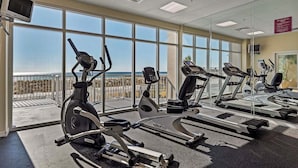 Una palestra con macchinari cardio, ampie finestre e vista sulla spiaggia.
