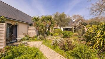 A residential property with a paved pathway, various shrubs, and a house with a sloped roof.