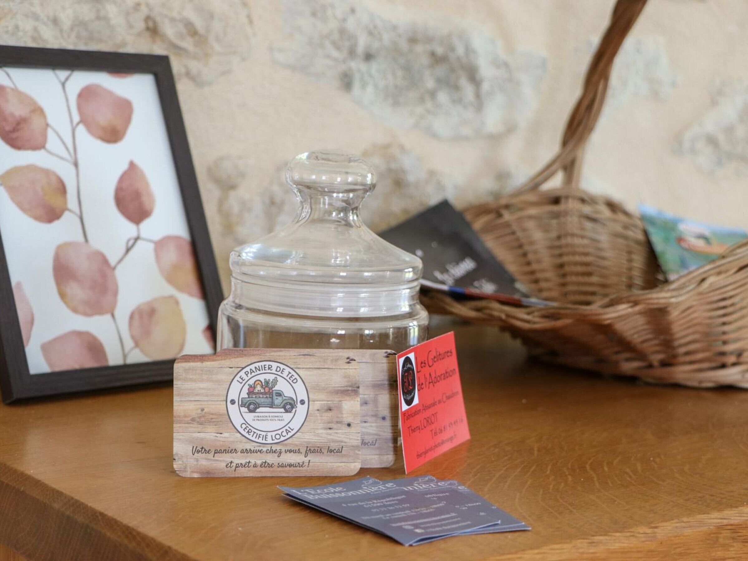 Een houten pot met een etiket, een lijst met een foto en een mandje op een houten ondergrond.