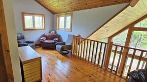 Avoin, loft-tyylinen huone, jossa on puulattia, puinen portaikko ja kaksi ikkunaa, joista on näkymä ulos.