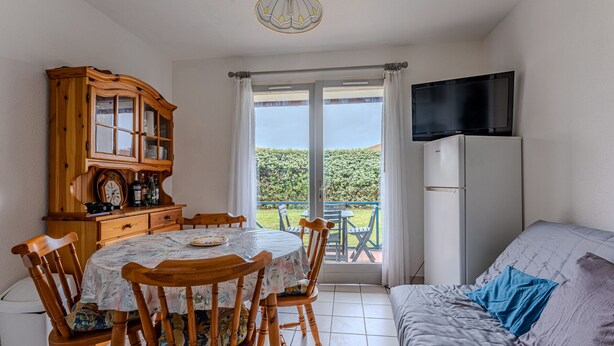 Een kamer met een eettafel, stoelen, een kast, een televisie en een bank.
