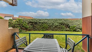 Een terras met een tafel en stoelen, een groene haag en een heldere lucht.
