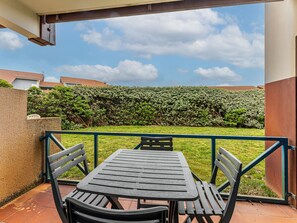 Eine Terrasse mit Tisch und Stühlen, ein grüner Heckenstreifen und ein klarer Himmel.