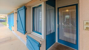 Een gebouw met een overdekte veranda, blauwe luiken en een nummer op de deur.