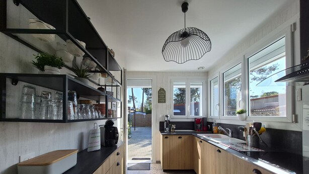 A modern kitchen with wooden cabinets, a black countertop, and a hanging pendant light. - Renovated house with enclosed garden - 8 guests (Saint-Brevin-les-Pins)