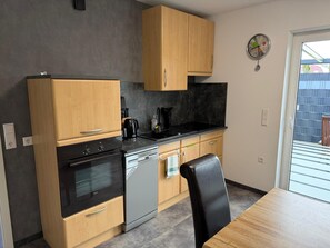 A compact kitchen with wooden cabinets, a black stove, a sink, and a dining table.