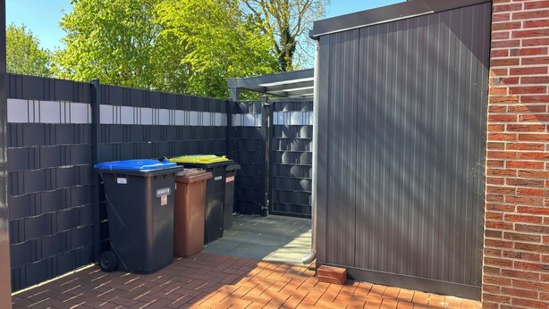 A fenced outdoor area with trash bins and a metal gate.