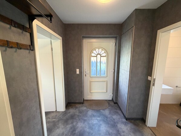 Un pasillo con una puerta que da a una habitación, una ventana pequeña con un diseño decorativo y una lámpara en el techo.