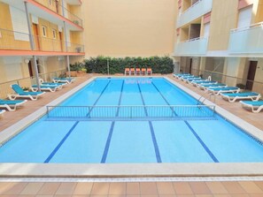 A swimming pool with multiple lanes, surrounded by lounge chairs and a building with balconies. - Apartamento en Calafell Cerca de la Playa (Calafell)