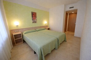 A room with two beds, a wooden nightstand, a wall-mounted light, and a door. - Apartamento en Calafell Cerca de la Playa (Calafell)