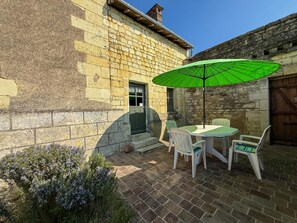 Ein Steinhaus mit einer Terrasse, auf der sich ein Tisch und Stühle unter einem grünen Sonnenschirm befinden.