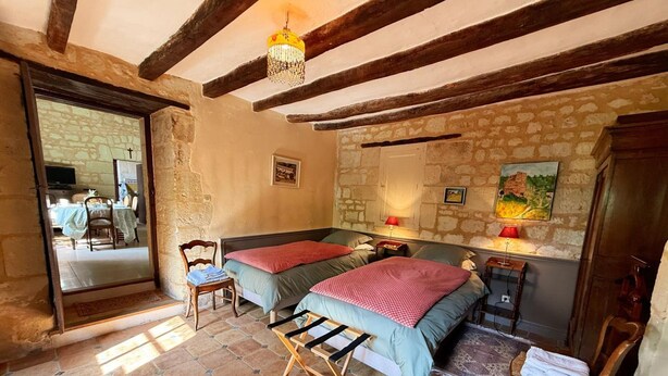 Ein Zimmer mit zwei Betten, einer Holzleiter, einem Essbereich mit Stühlen und einer Steinwand.