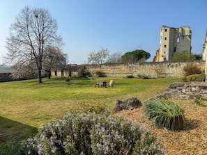 A historic stone building with a grassy courtyard, a swing set, and a large tree.