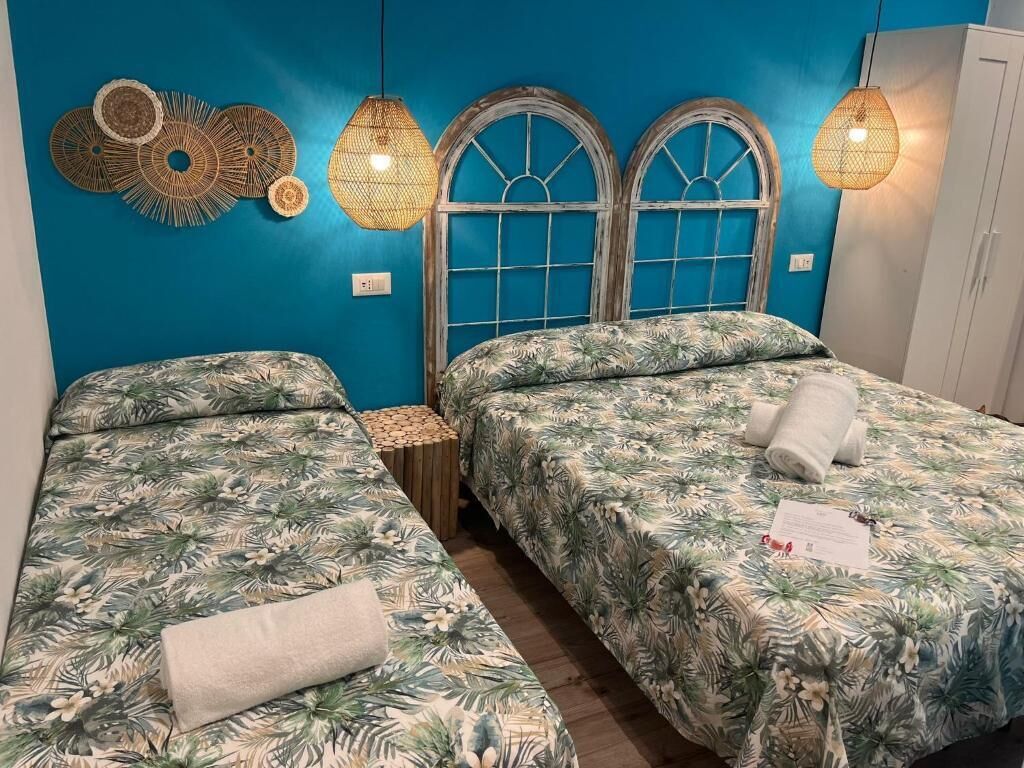 Une chambre avec deux lits, une table de chevet en bois et un mur bleu orné d’œuvres d’art décoratives.