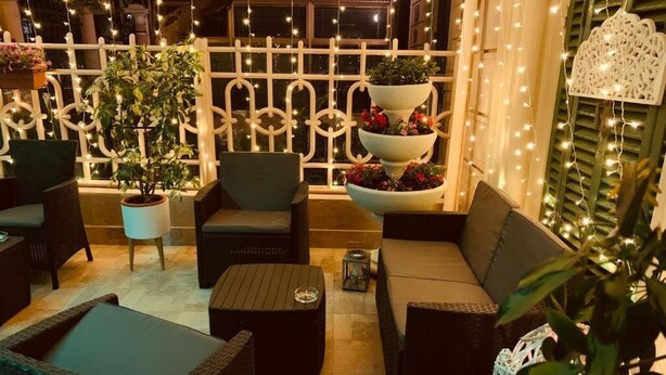 En utomhusplats med sittmöbler i rotting, en trappstegsformad blomlåda och ljusslingor.