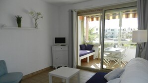 Et værelse med en seng, et fjernsyn på et lille skab, et bord, en stol og en balkon med et bord og stole.