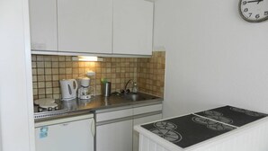 Et kompakt køkken med hvide skabe, kaffemaskine, elkedel og vask.