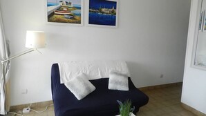 Et værelse med en mørkeblå sofa, to puder, en hvid lampe og to billeder i rammer på væggen.