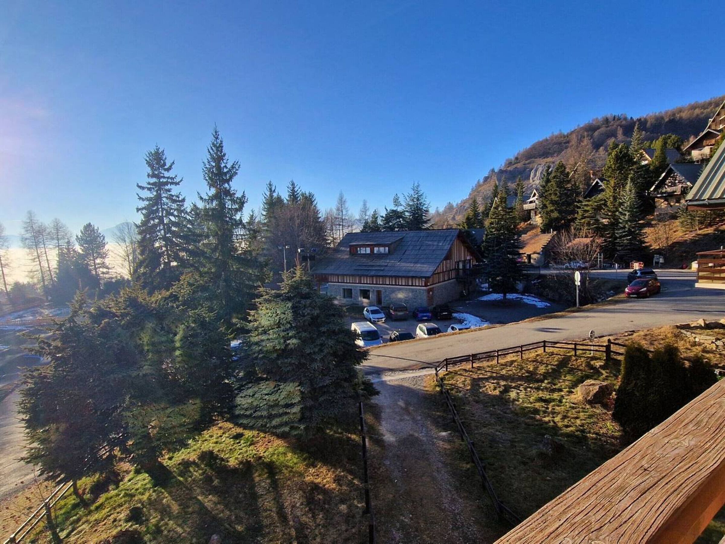 A mountain lodge with a parking area, surrounded by trees and a view of a mountain.